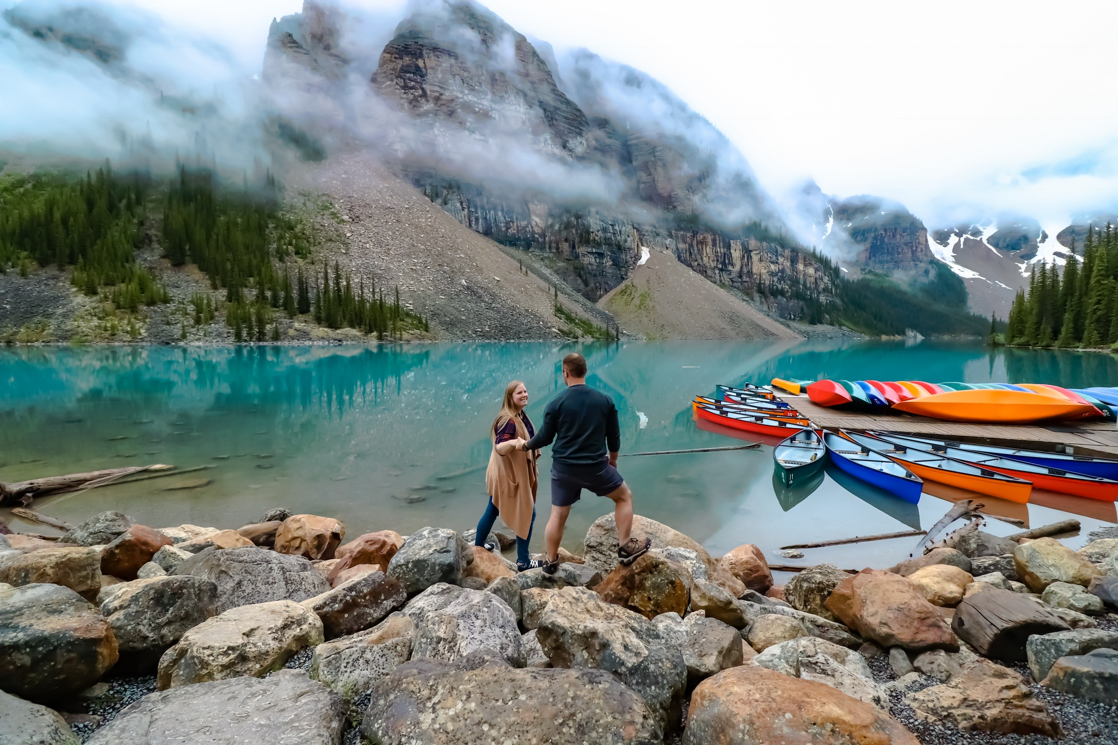 Couple in front of icy blue water of Moraine Lake in Banff | Traveling Twogether